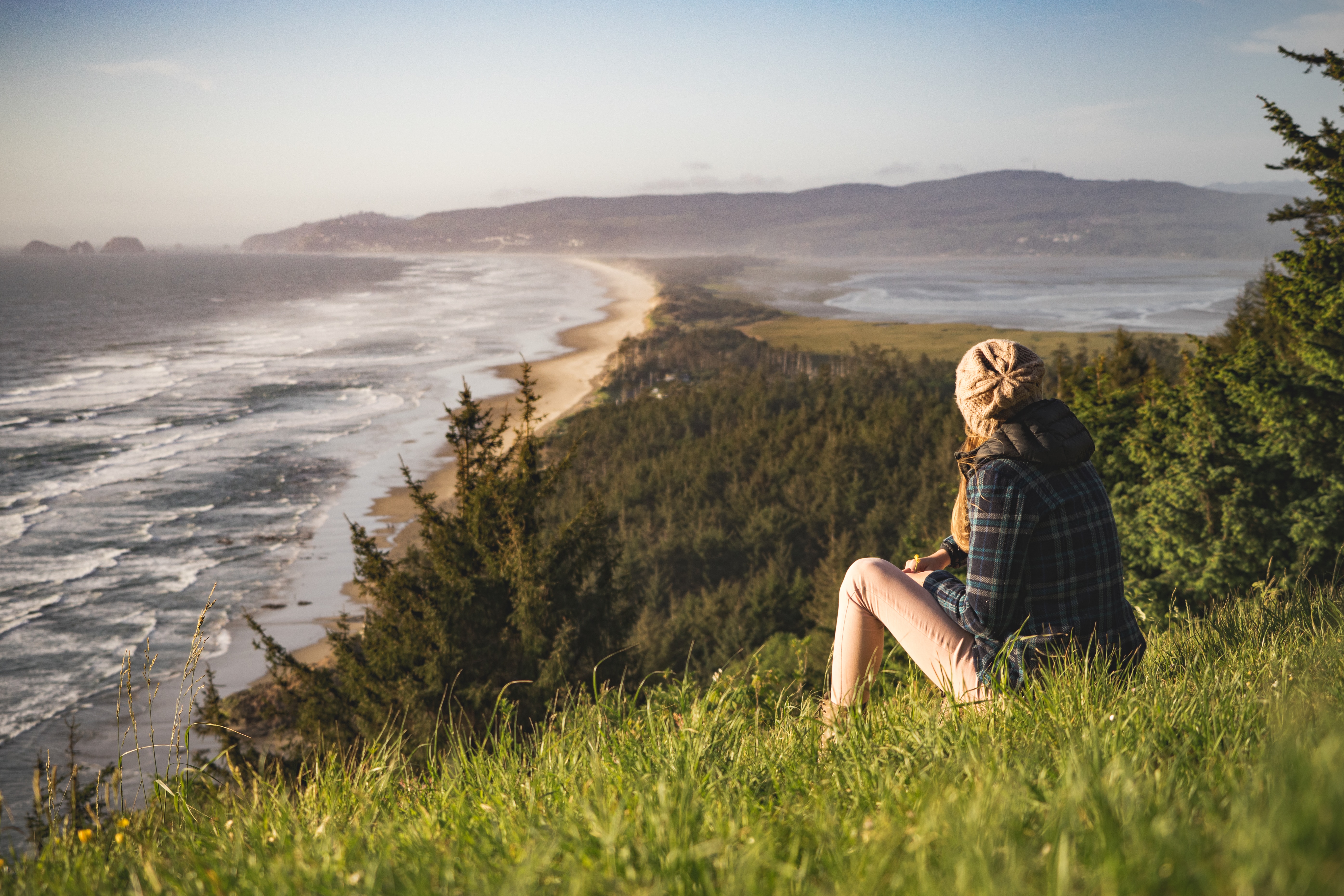 Frau sitzt auf einem Hügel und blickt auf den Strand.